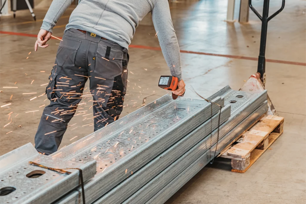 Monteur slijpt gegalvaniseerde staalbalk met vonkenregen als onderdeel van montagevoorbereiding.